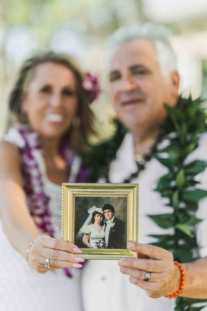 Vow renewal couple posing with their original wedding photo on Oahu